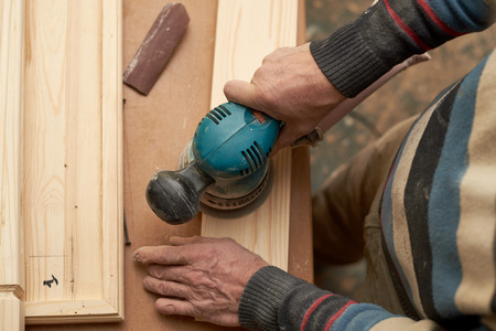A man treats a wooden product with a grinding machine. Circular grinding machine light wood.
