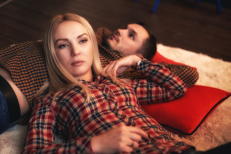 The girl lies on the guy and they look thoughtfully in different directions. A couple in love lies on red pillows.の写真素材