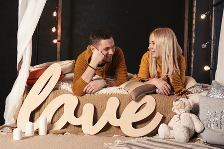 A couple in love lies on the bed and look at each other. The inscription love in the foreground.の写真素材