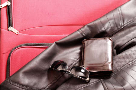 Ready to travel. A suitcase with glasses, wallet and a leather jacket.