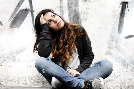 A young woman listening to melancholic Music and sitting on the pavement 