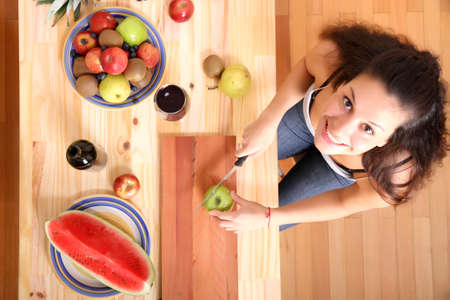 A young adult woman cutting fruits in the kitchen の写真素材