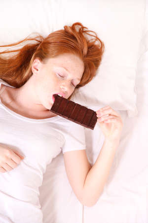 A young redhead woman eating Chocolate in Bed.
の写真素材
