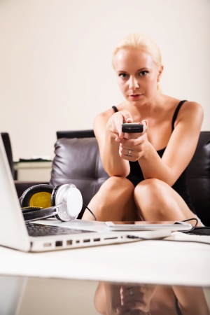 A blonde girl watching TV with the remote control in her hands
の写真素材