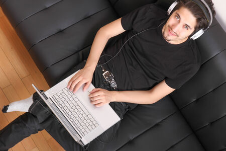 A young hispanic man with a laptop on the Sofa listening Music with headphones の写真素材