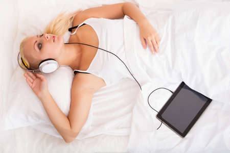 Portrait of a blonde girl lying in a bed listening to music.の写真素材