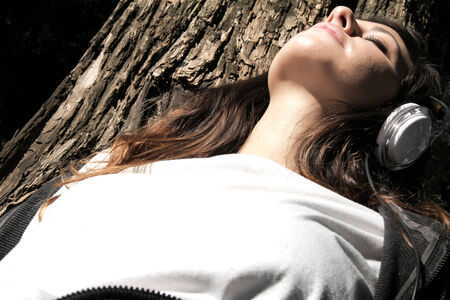 A young woman enjoying Music and sitting on a branch.の写真素材