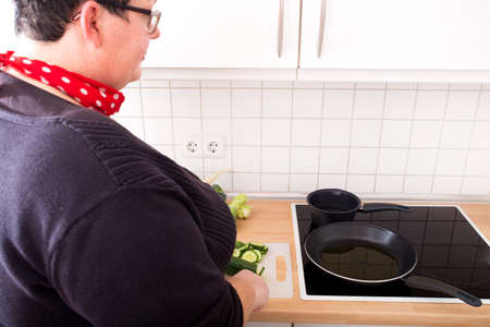 Mature overweight woman cutting cucumber in the kitchen.の写真素材
