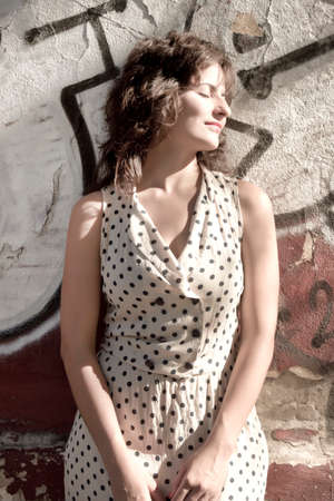 A vintage style dressed girl leaning at a graffiti wall and enjoying the sunlight.のeditorial素材