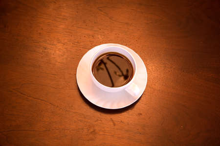 A classical cup of coffee on a dark wooden desk.の写真素材