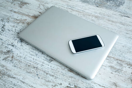 A Smartphone and a switched off laptop computer on a wooden Desktop.