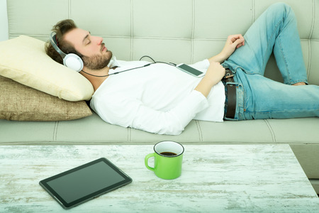 A young Hipster listening music with a smartphone on a sofa with headphones.の写真素材