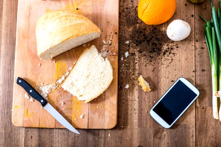 A smartphone lying in a natural kitchen with white bread spices olives and spring onions.の写真素材