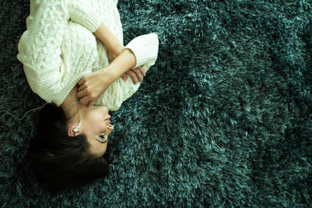 A young beautiful woman in underwear lying on a carpet and listening to musicの写真素材
