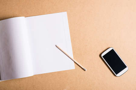 A smartphone and a exercise book on a wooden Desk.の写真素材