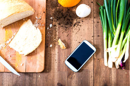 A smartphone lying in a natural kitchen with white bread, spices, olives and spring onions.の写真素材