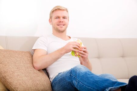 Young man with a Sandwich on the Sofaの写真素材