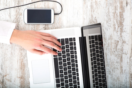 A young man using his laptop computer and various other devices on a desktop.の写真素材