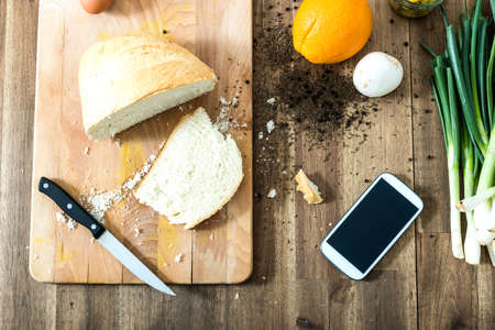 Retro picture of a smartphone lying in a natural kitchen with white bread, spices, olives and spring onions.の写真素材