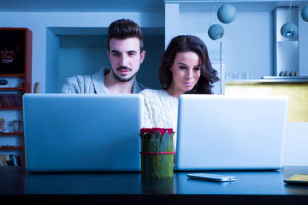 A young couple in the evening using their laptop computers at home.の写真素材