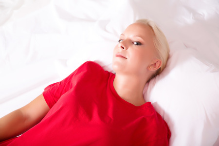 A young blonde woman wearing a red shirt and lying on the bed.の写真素材