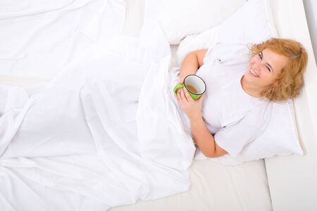 A young plus size woman drinking the first coffee of the day in bed.の写真素材