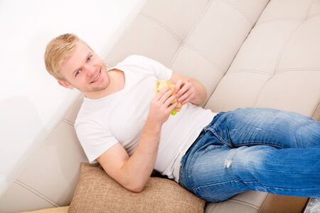 Young man eating a sandwich at homeの写真素材