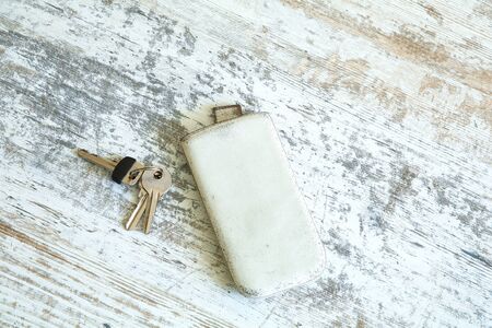 Keys and a smartphone in a leather case on a wooden table.