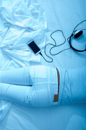 A young, beautiful woman relaxing in the bed with headphones and a smartphone