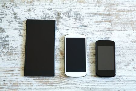 Three smartphone in different sizes on a wooden table.