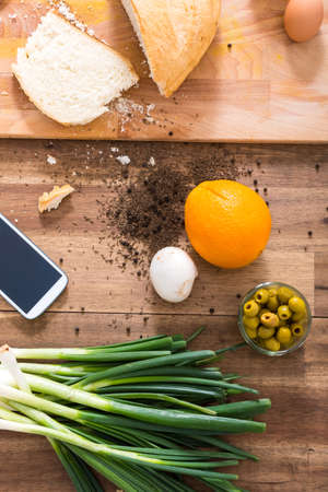 A smartphone lying in a natural kitchen with white bread, spices, olives and spring onions.の写真素材