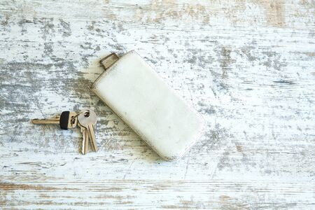 Keys and a smartphone in a leather case on a wooden table.の写真素材