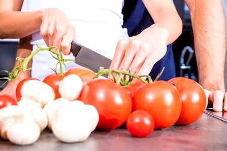 Beautiful young couple cooking while enjoying a glass of wine in the kitchen.の写真素材