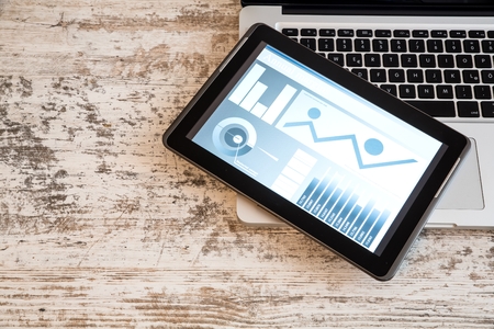 Business Analytics on a wooden Desk with a Tablet PC and a Laptop.
