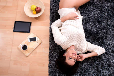 A young beautiful woman in underwear lying on a carpet and listening to musicの写真素材