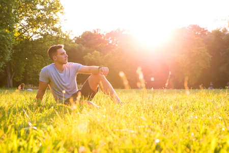 A handsome young man relaxing in the sunset and sitting in the grass.の写真素材
