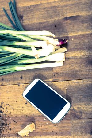 A smartphone lying in a natural kitchen with white bread, spices, olives and spring onions.の写真素材