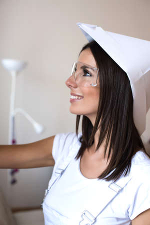 Beautiful young woman painting her Apartment with safety glasses and a paper hat.の写真素材