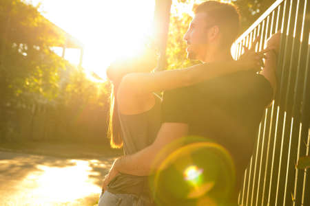 A young HipHop styled couple hugging next to a fence during sunset in a urban environment.の写真素材