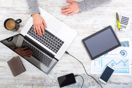 A working woman's hand at a table with laptop,tablet and phone.