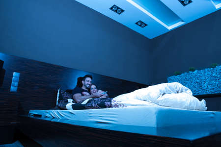 Beautiful young couple watching TV in Bed at night.の写真素材