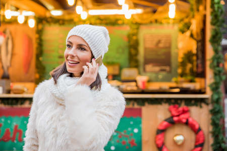 A beautiful young woman talking on the phone on the christmas market.の写真素材