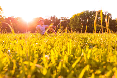 A handsome young man relaxing in the sunset and sitting in the grass.の写真素材