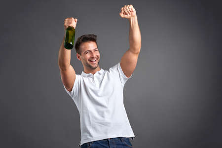 A handsome young man feeling happy and celebrating while holding a beerの写真素材