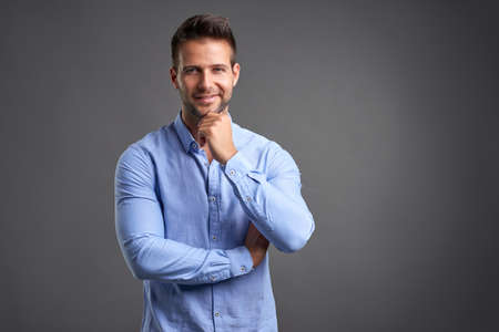 A confident handsome young man standing in front of a grey background in a studioの写真素材