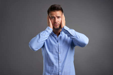 A handsome young man feeling stressed and grabbing his head in a studioの写真素材