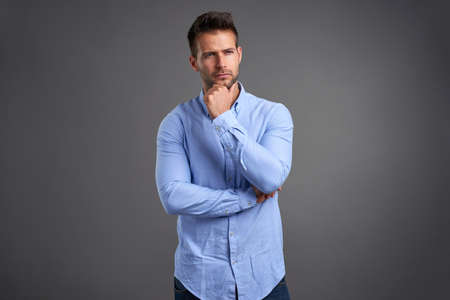 A handsome young man thinking in front of a grey background in a studioの写真素材
