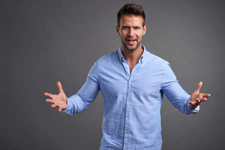 A handsome young man looking uncomprehendingly in to the camera in front of a grey background in a studioの写真素材