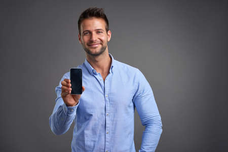 A confident handsome young man showing his phone to the camera