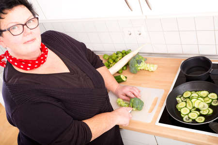 Mature overweight woman cutting vegetables in the kitchen.
の写真素材